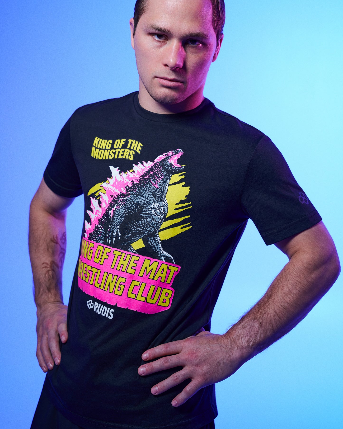 A man wearing a black graphic t-shirt with a Godzilla design and text, posed against a blue gradient studio background.