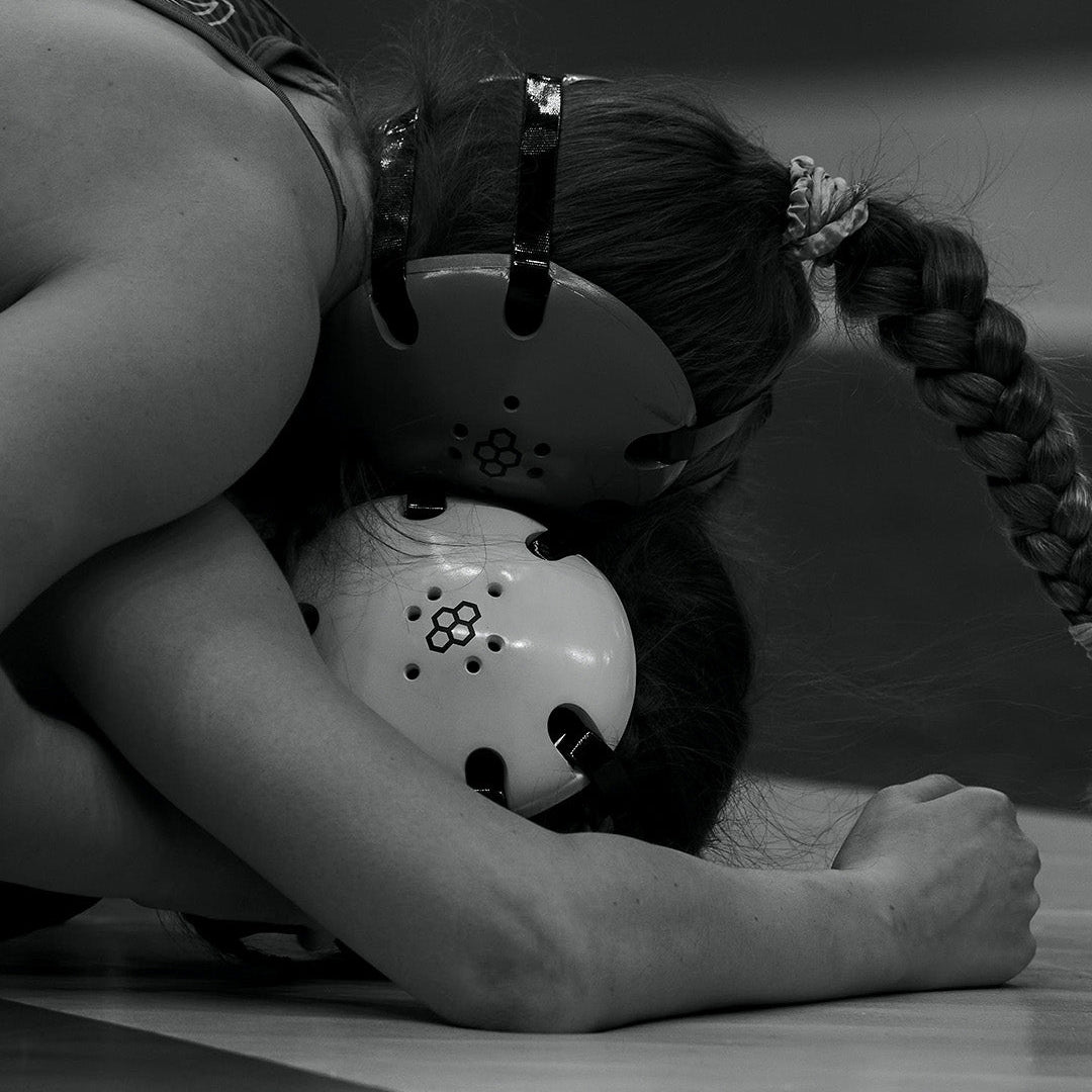 Black and white action shot of women’s wrestlers competing on the mat, both wearing RUDIS headgear, capturing intensity, resilience, and the spirit of wrestling competition.