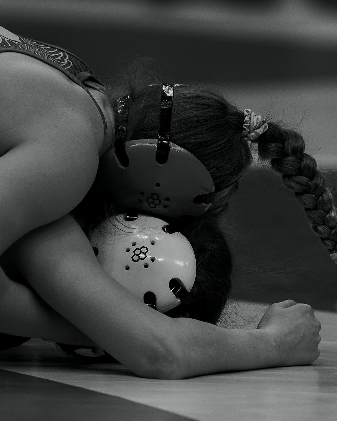 Black and white action shot of women’s wrestlers competing on the mat, both wearing RUDIS headgear, capturing intensity, resilience, and the spirit of wrestling competition.