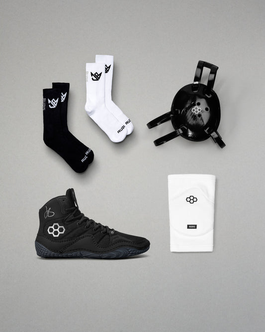 Black and white socks, black wrestling shoes, and a headgear on a gray background.