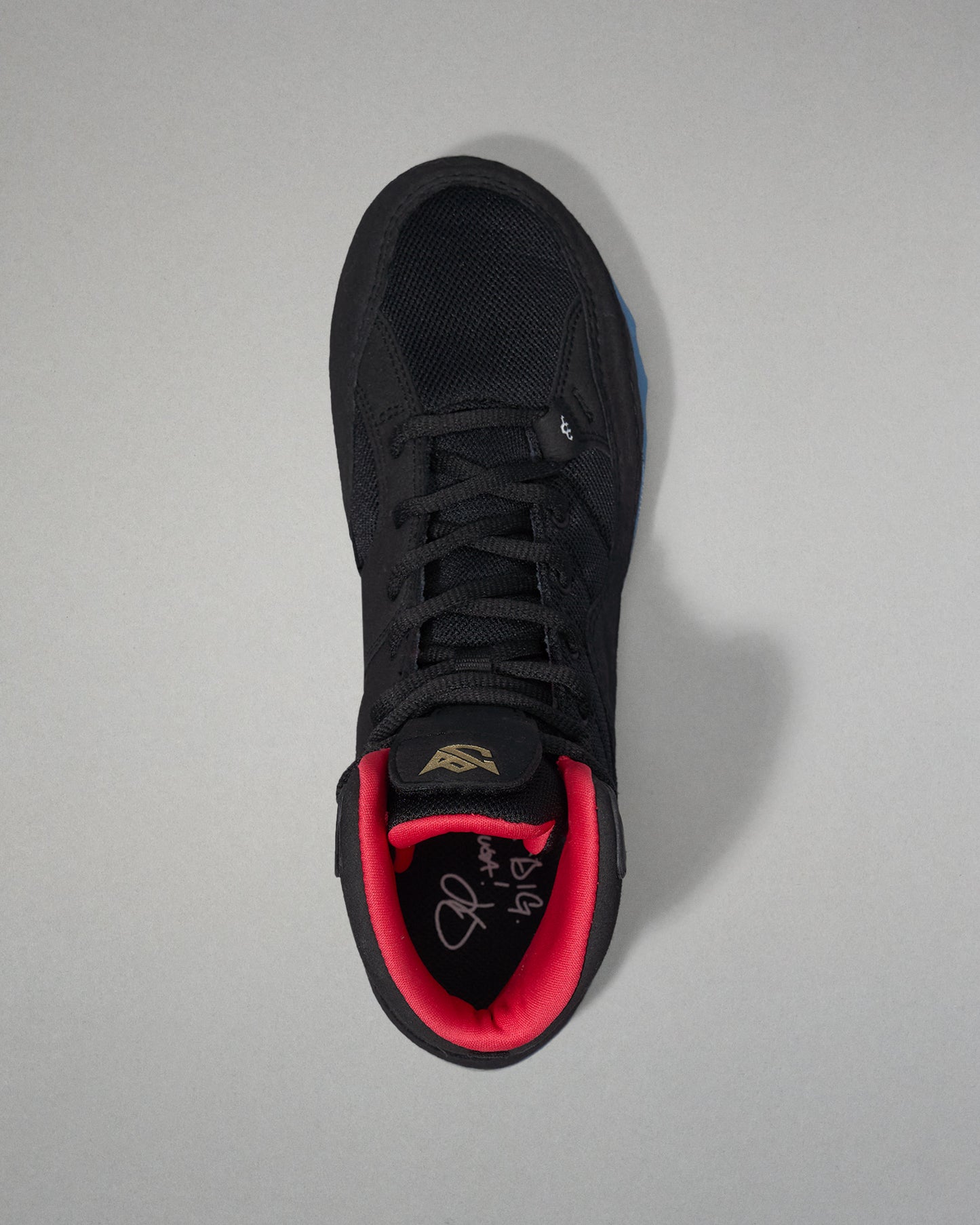 Black wrestling shoe with red lining on a gray background