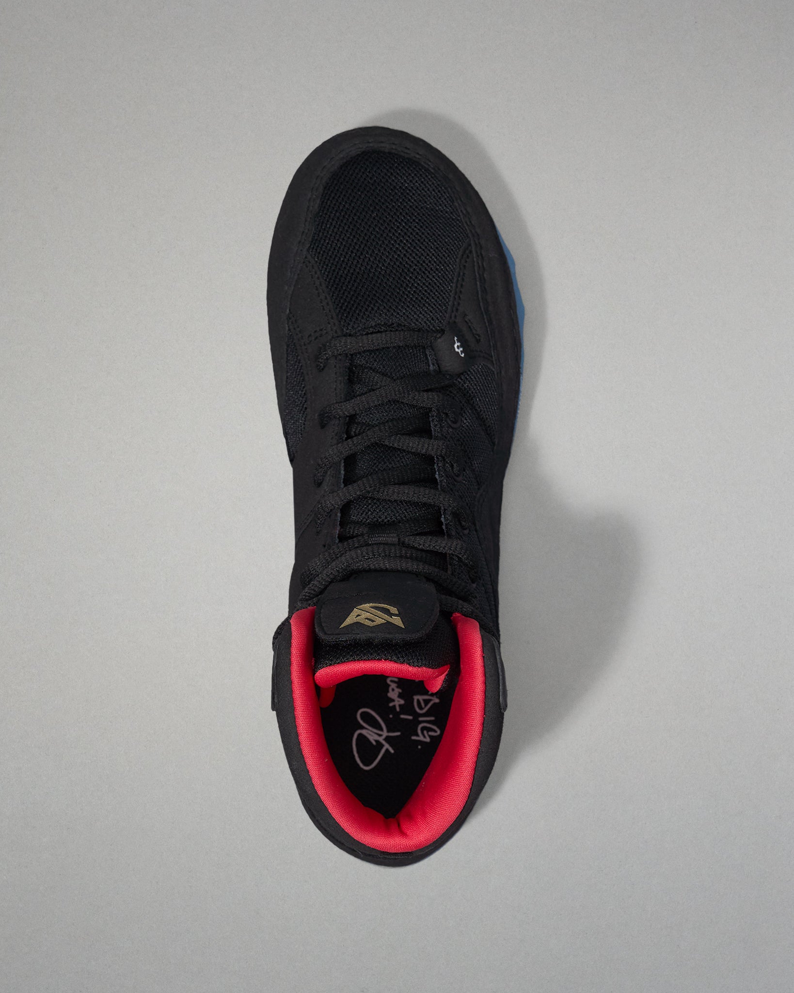 Black wrestling shoe with red lining on a gray background