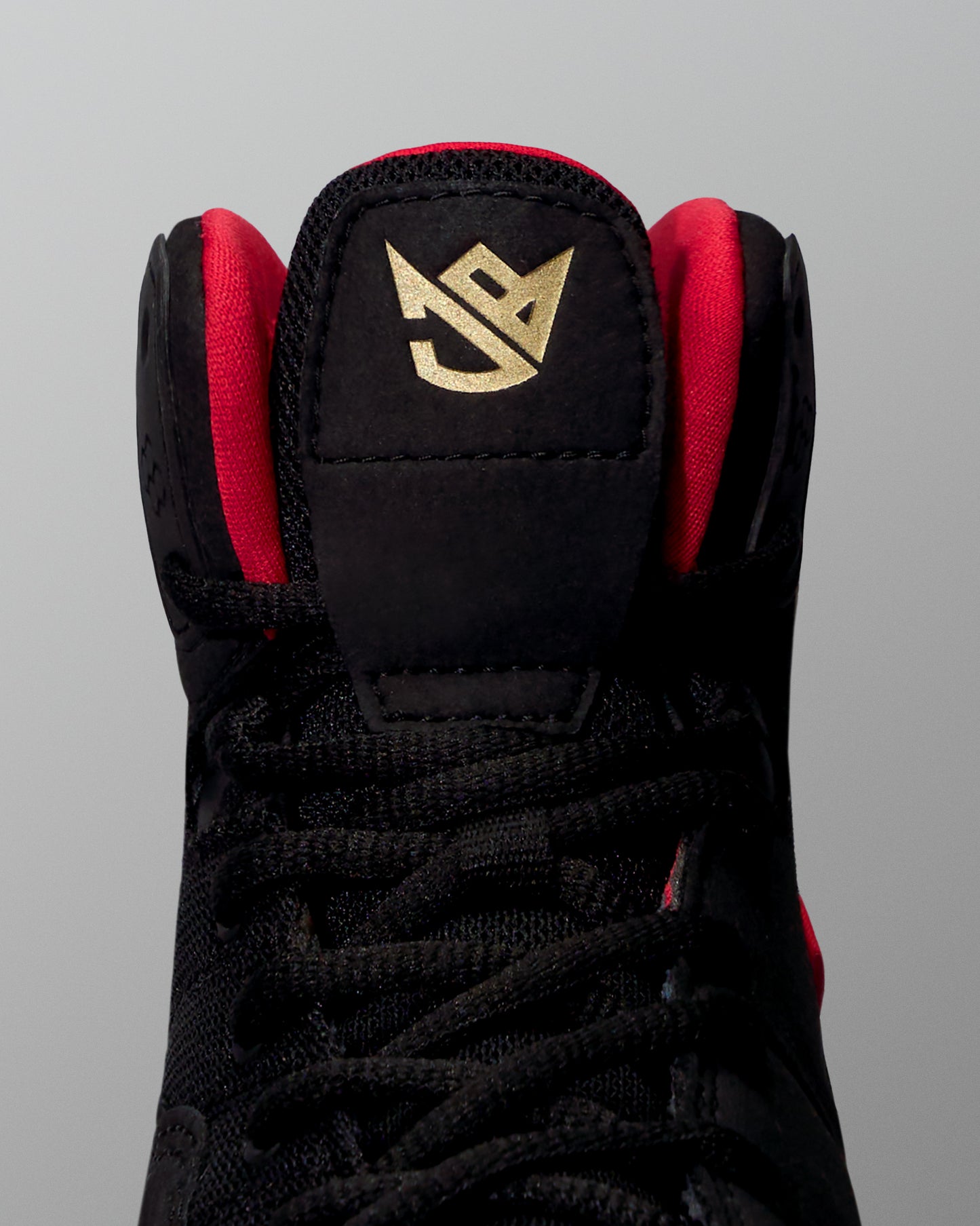 Black wrestling shoe with red accents and a gold logo on a gray background