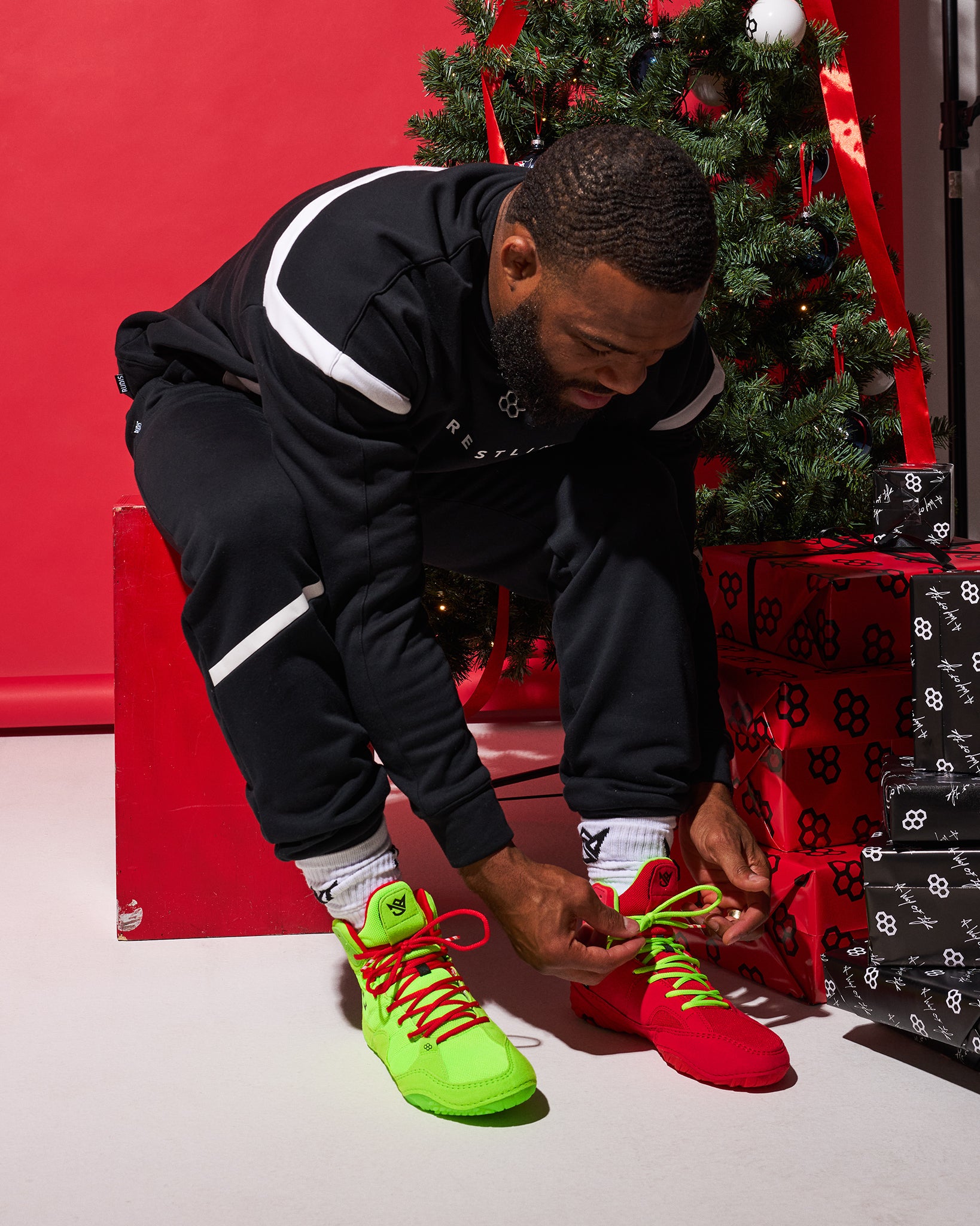 Person tying bright green and red sneakers in front of a Christmas tree and presents.