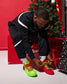 Person tying bright green and red sneakers in front of a Christmas tree and presents.