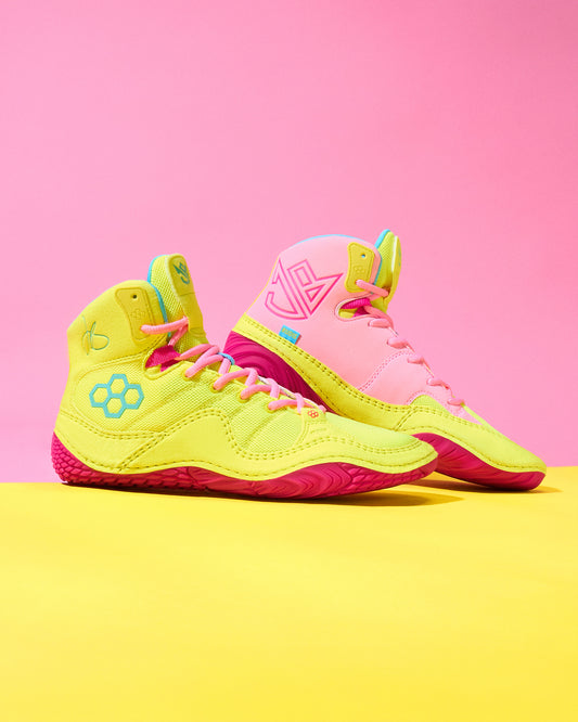 Pair of neon yellow and pink wrestling shoes on a pink and yellow background