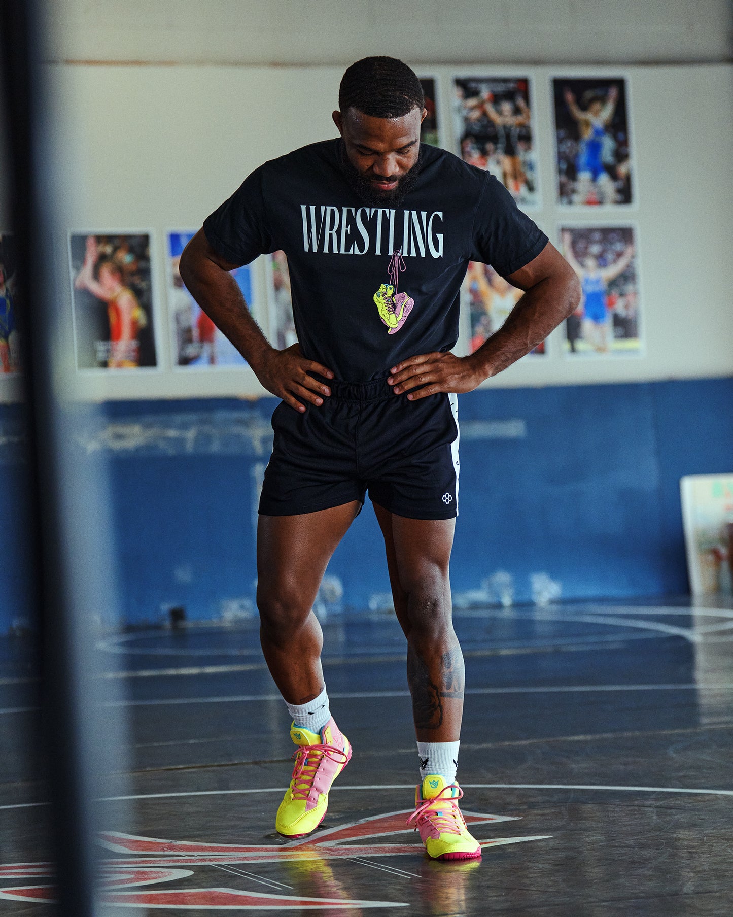 Person wearing a 'Wrestling' shirt in a gym setting with posters on the wall.