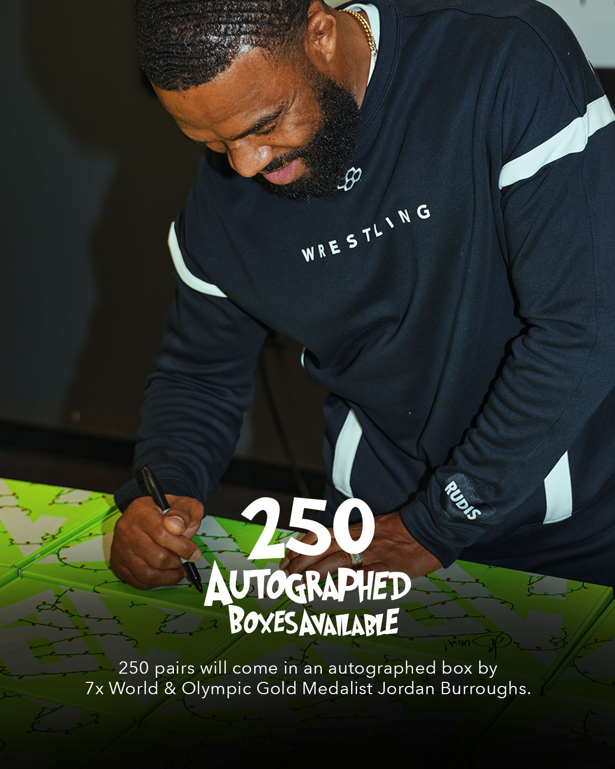 Man in a wrestling-themed sweatshirt signing shoe boxes