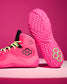 A pair of bright pink athletic wrestling shoes with neon yellow-green laces and a black hexagonal logo, shown on a matching pink studio background. One shoe is positioned upright to display the textured sole, and the other is angled to show the side profile.