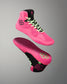 A pair of high-top athletic wrestling shoes in bright pink and black, shown floating against a neutral gray gradient background. One shoe is oriented to show the side profile with neon green laces, while the other shows the sole with a matching pink and black tread pattern.