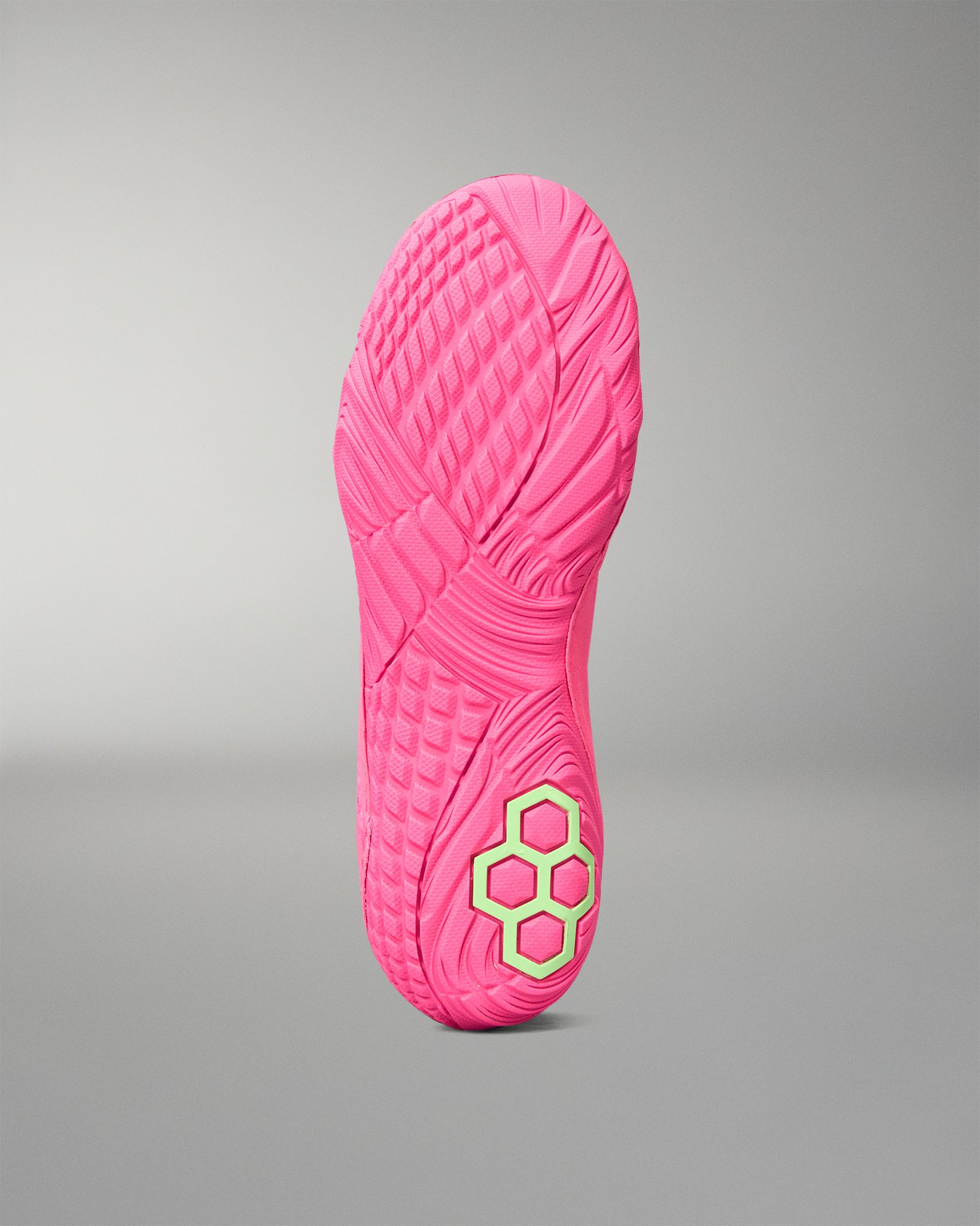 A bright pink wrestling shoe sole shown upright against a neutral gray gradient background, featuring a textured tread pattern and a small lime green hexagonal logo near the heel.