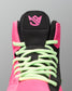 Close-up of a high-top wrestling shoe showing the tongue, laces, and side panels in bright pink, black, and neon green on a gray background.