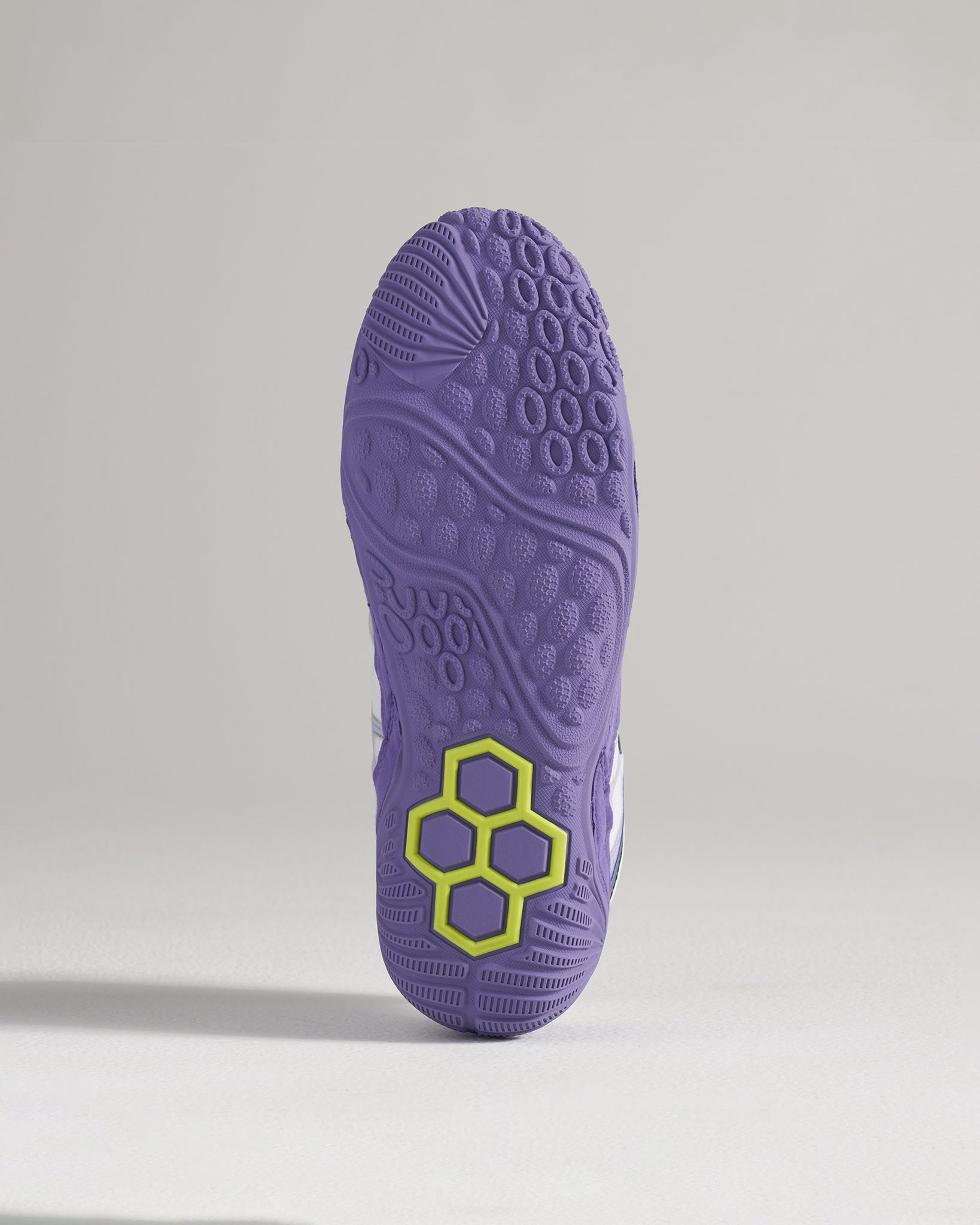 A detailed view of a purple athletic shoes outsole showcasing a unique tread pattern and a distinct hexagonal logo in green