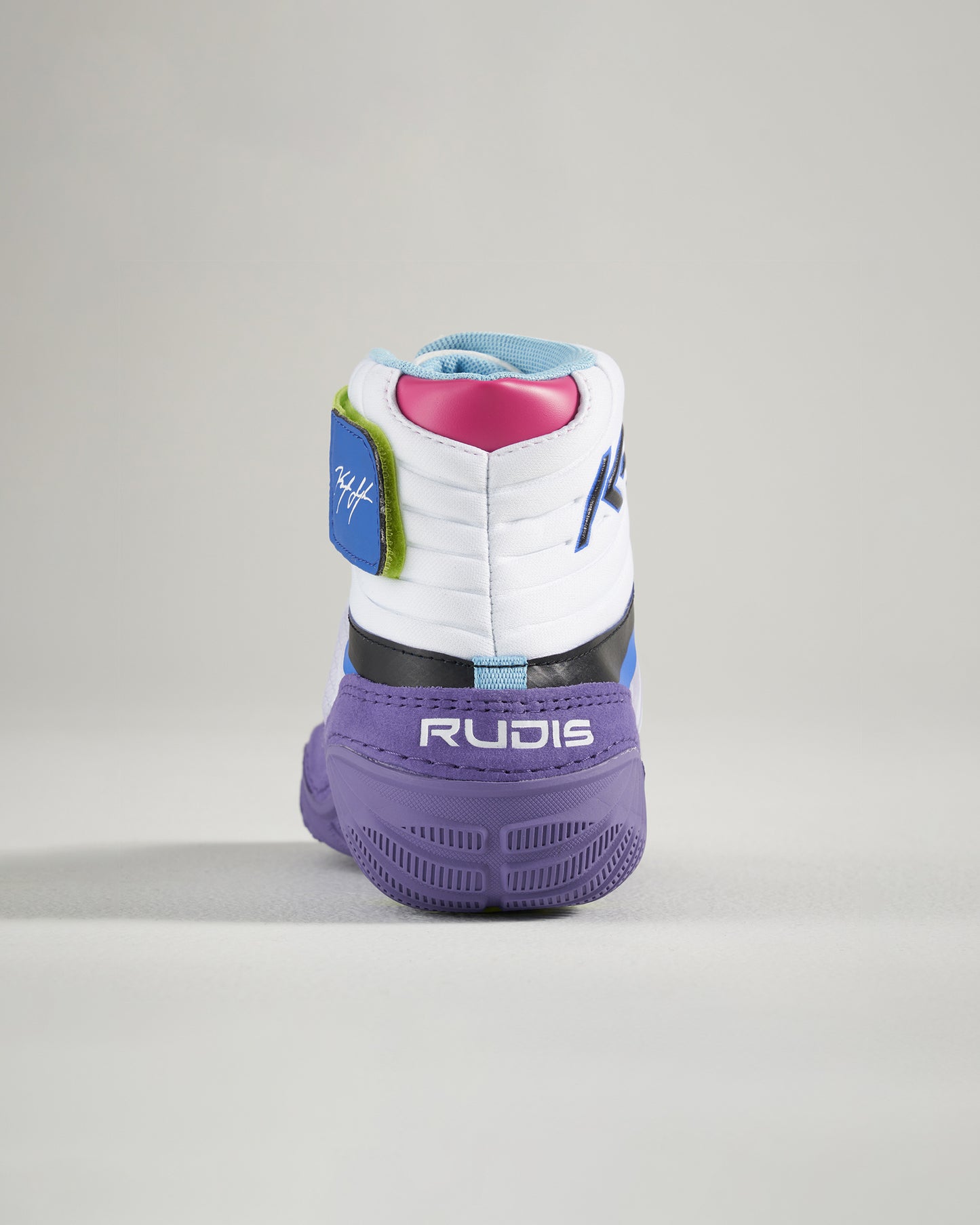 A vibrant wrestling shoe with a predominantly white body highlighted by colorful accents in blue green pink and purple featuring the brand name RUDIS prominently displayed on the heel