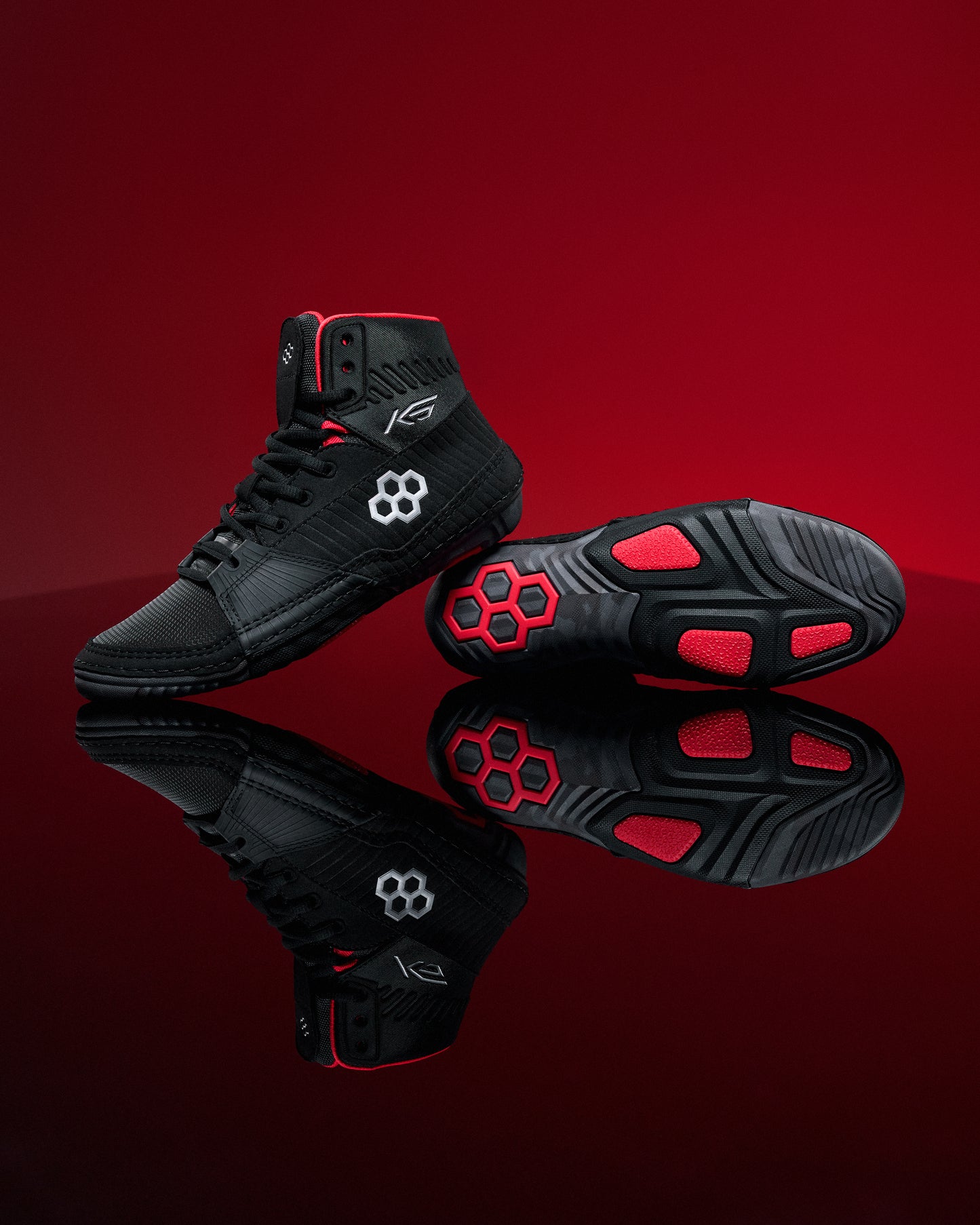 Black wrestling shoes with red accents on a reflective red surface