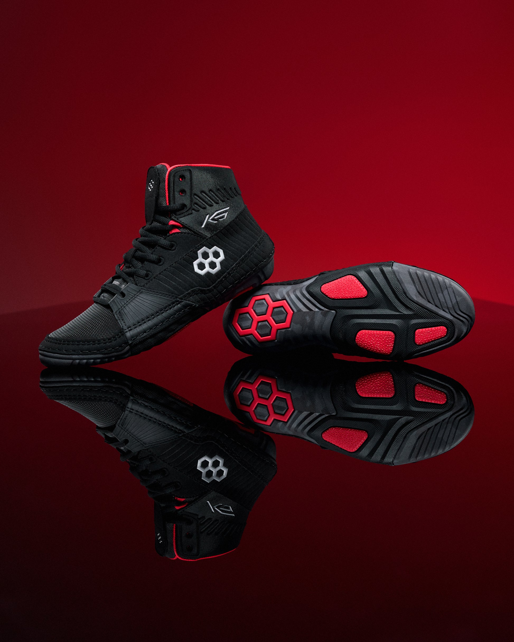 Black wrestling shoes with red accents on a reflective red surface