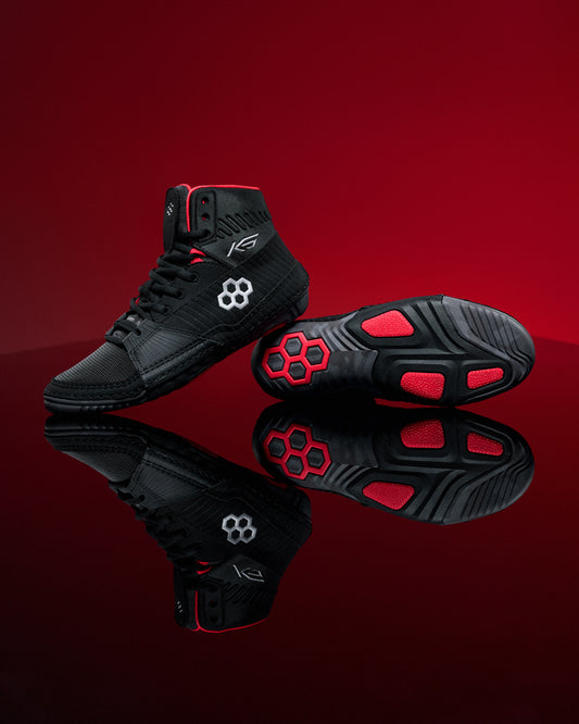 Black wrestling shoes with red accents on a reflective red surface