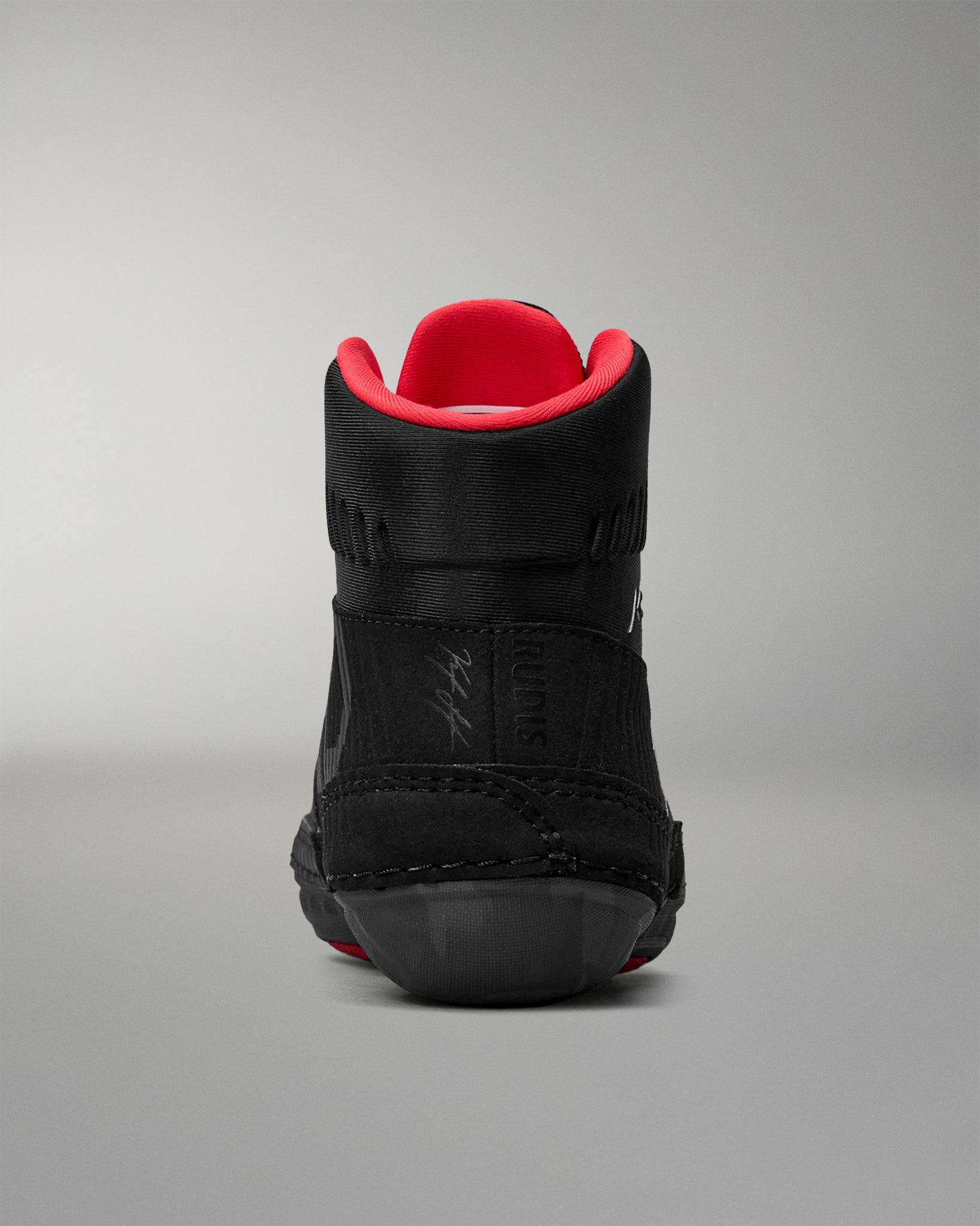 Black wrestling shoe with red lining on a gray background