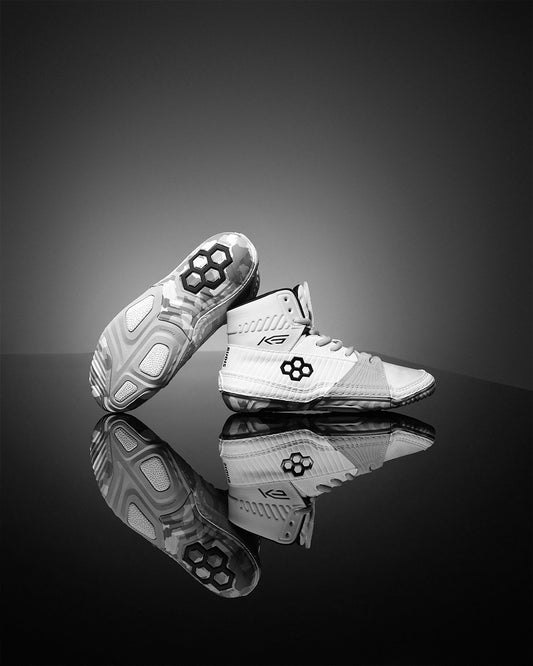 Pair of white wrestling shoes with black sole design on a reflective surface.