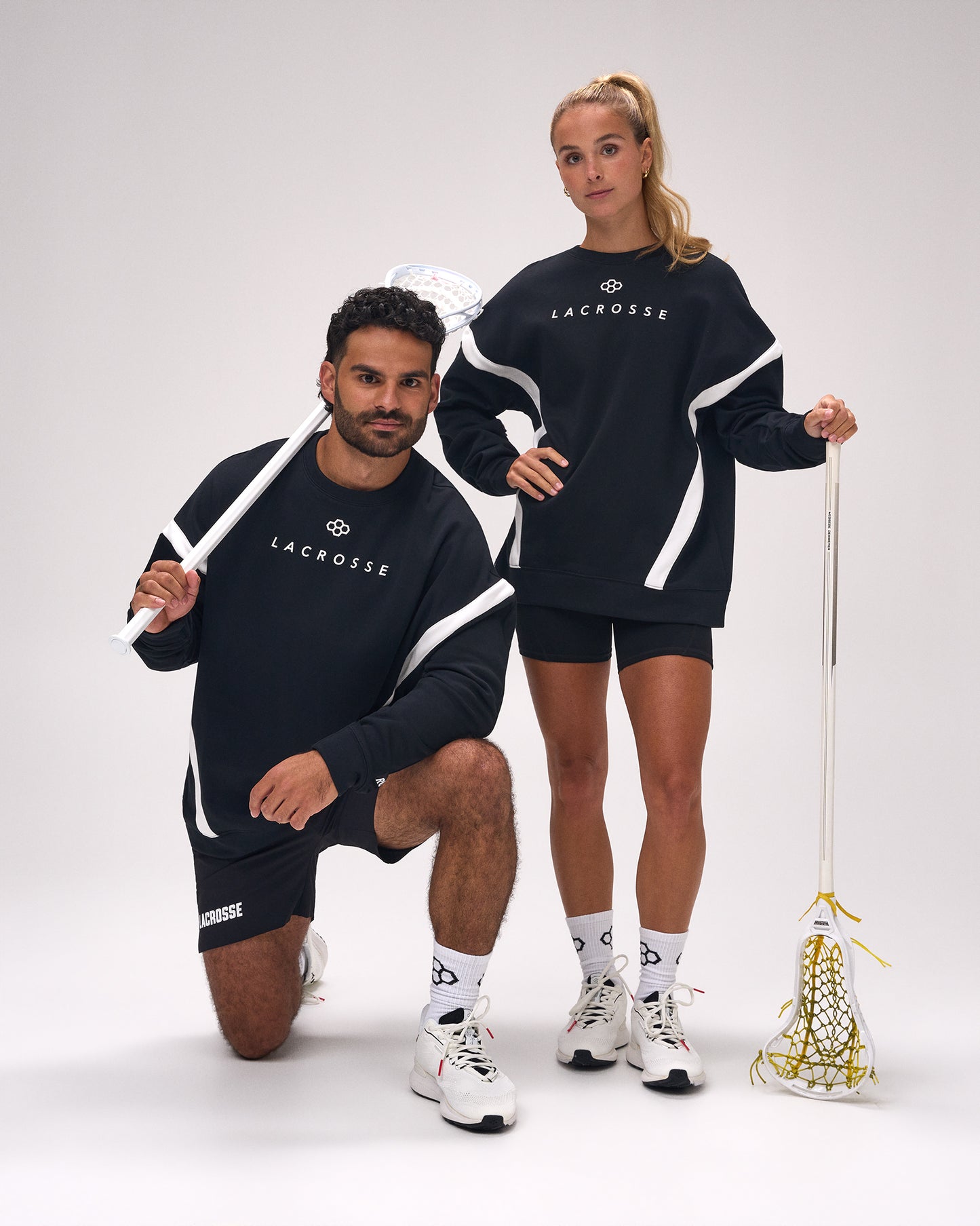Male and female athletes wearing the RUDIS Lacrosse Colorblock Crewneck in Blackout, showcasing premium athletic fleece with modern colorblock panels while holding lacrosse sticks.