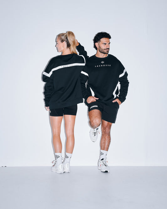 Front and back lifestyle view of the RUDIS Lacrosse Colorblock Crewneck in Blackout featuring contrast colorblock panels, minimalist Lacrosse chest graphic, and "A Way of Life" back detail.