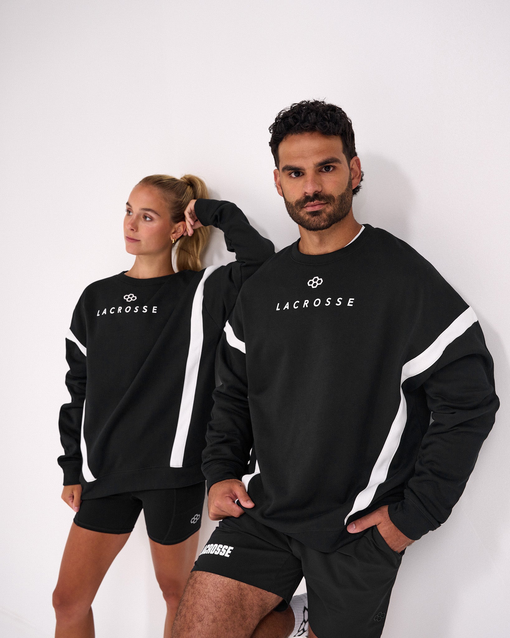 Male and female athletes wearing the RUDIS Lacrosse Colorblock Crewneck in Blackout featuring premium heavyweight fleece, bold colorblock paneling, minimalist Lacrosse chest graphic, and relaxed athletic fit.