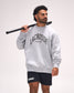 A man wearing a light gray crewneck sweatshirt with 'LACROSSE' printed in black across the chest, paired with black shorts, holding a lacrosse stick over his shoulder against a plain light background.