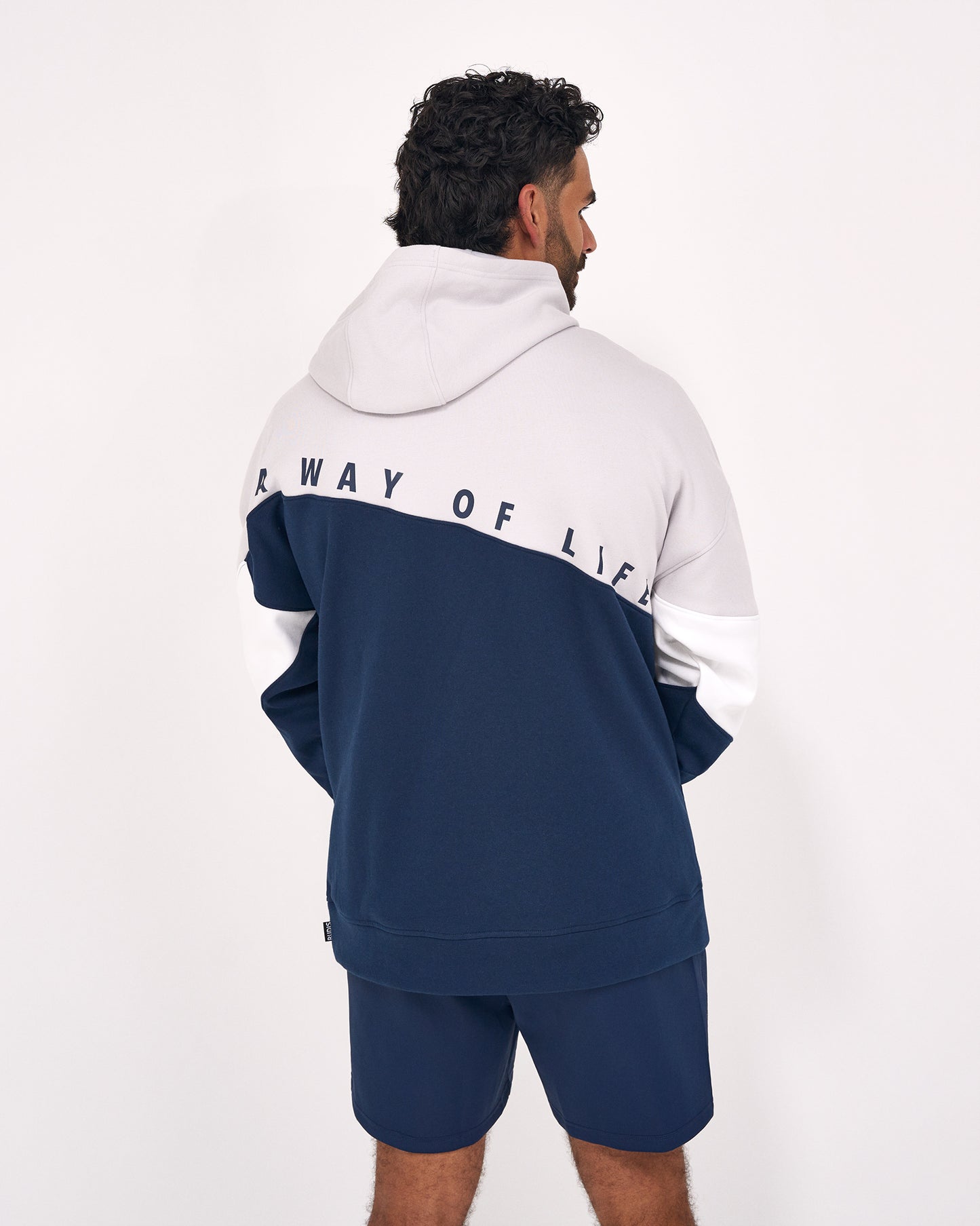 A man shown from the back wearing a color-blocked hoodie and matching shorts. The hoodie has a light gray upper section, white sleeves, and a navy blue lower section, with the text 'WAY OF LIFE' printed across the shoulders.