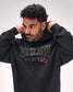 A man wearing a black hoodie with 'RESOLUTE LACROSSE' printed across the chest in metallic gold and red lettering, posing with his hands behind his head against a light gray background.
