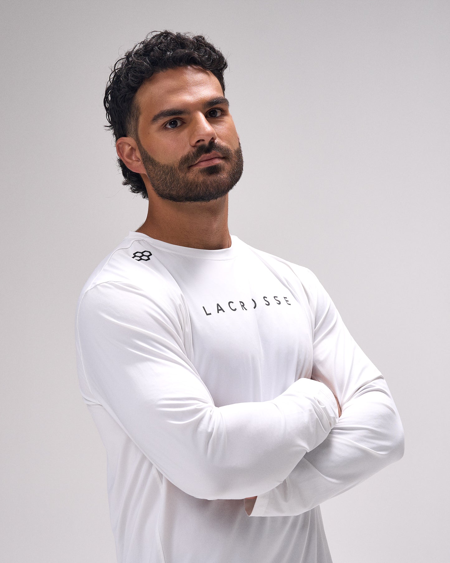 A man wearing a white long-sleeve athletic shirt with 'LACROSSE' printed across the chest and a small logo on the right shoulder, posed against a light gray studio background.