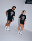 Male and female athletes wearing the RUDIS Motto Lacrosse Heavyweight T-Shirt in Black featuring a bold lacrosse head graphic, oversized fit, premium heavyweight cotton, and everyday athletic styling.