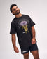 A man modeling a black Lacrosse brand t-shirt with a yellow and purple lacrosse graphic, paired with black shorts, against a light gray studio background.