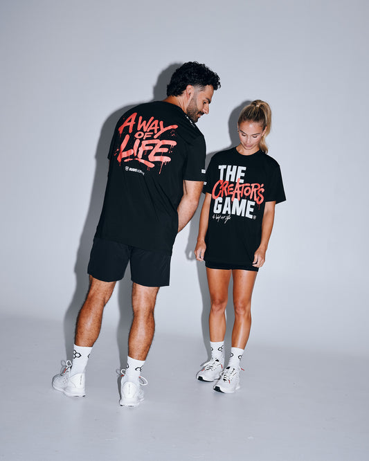 Male and female athletes wearing the RUDIS The Creator's Game Hybrid T-Shirt in black. The front features bold "The Creator's Game" artwork, while the back showcases oversized "A Way of Life" graphics inspired by lacrosse culture.
