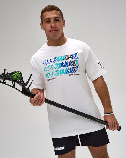 A man wearing a white lacrosse t-shirt with a blue and black graphic pattern, black lacrosse shorts, and holding a lacrosse stick with a green ball, against a light gray studio background.
