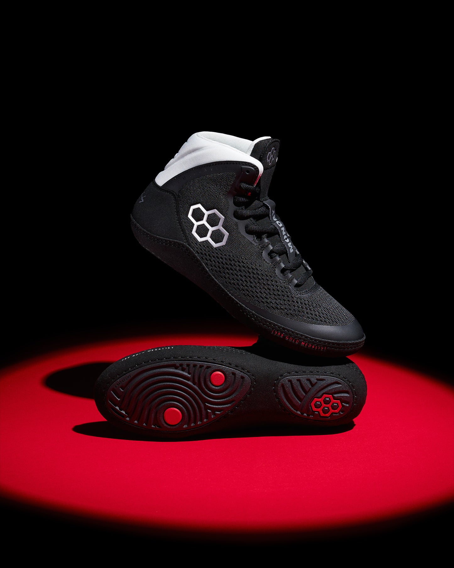 Black wrestling shoes with white accents on a red and black background
