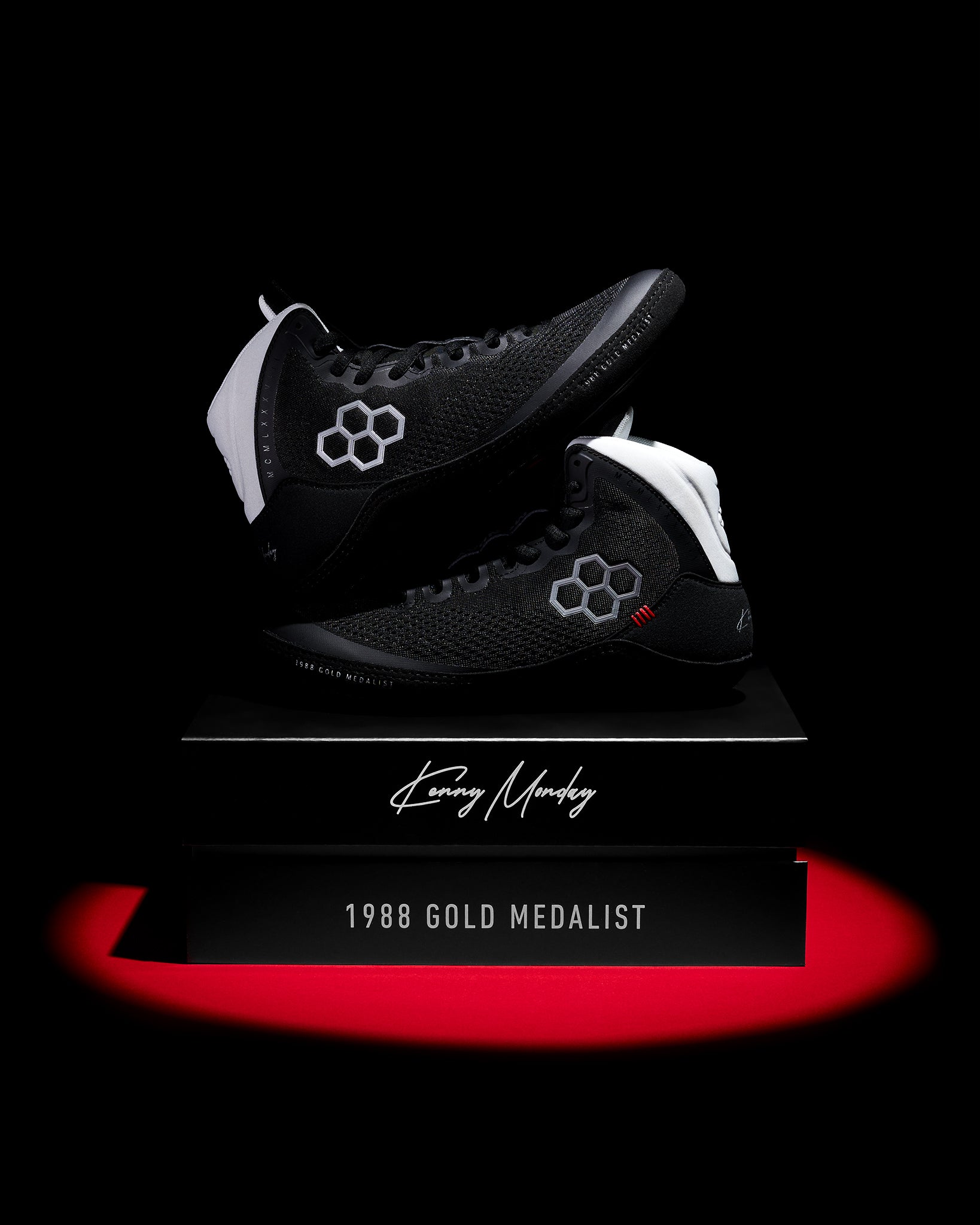 Black wrestling shoes with white accents on a black background, featuring a signature and text.