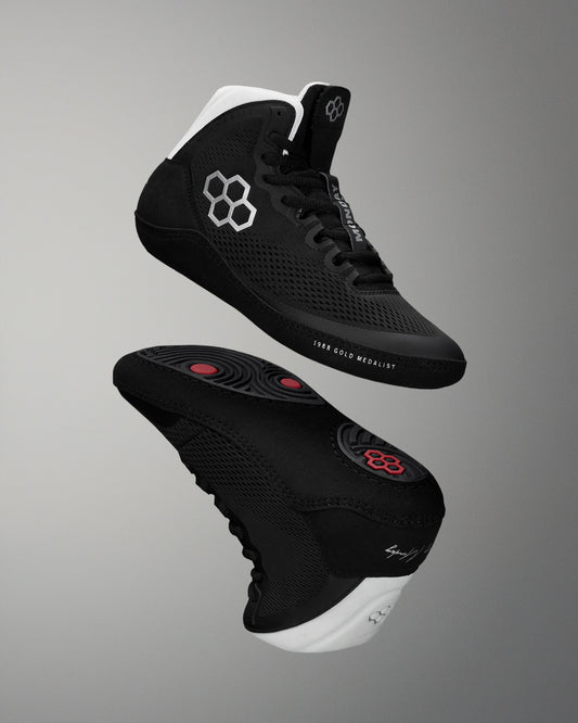 Black wrestling shoes with white soles on a gray background