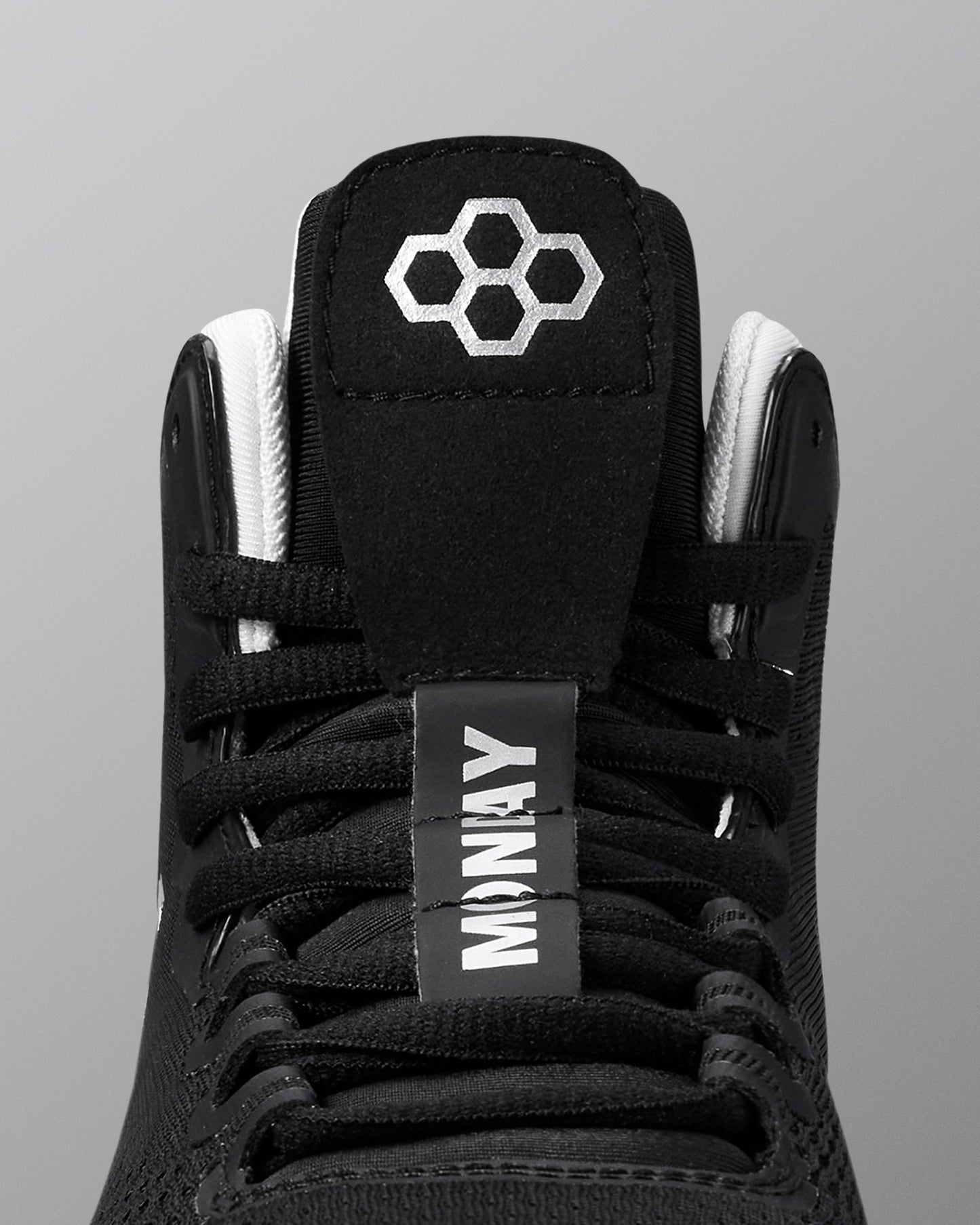 Black wrestling shoe with white laces and a visible brand logo on a gray background