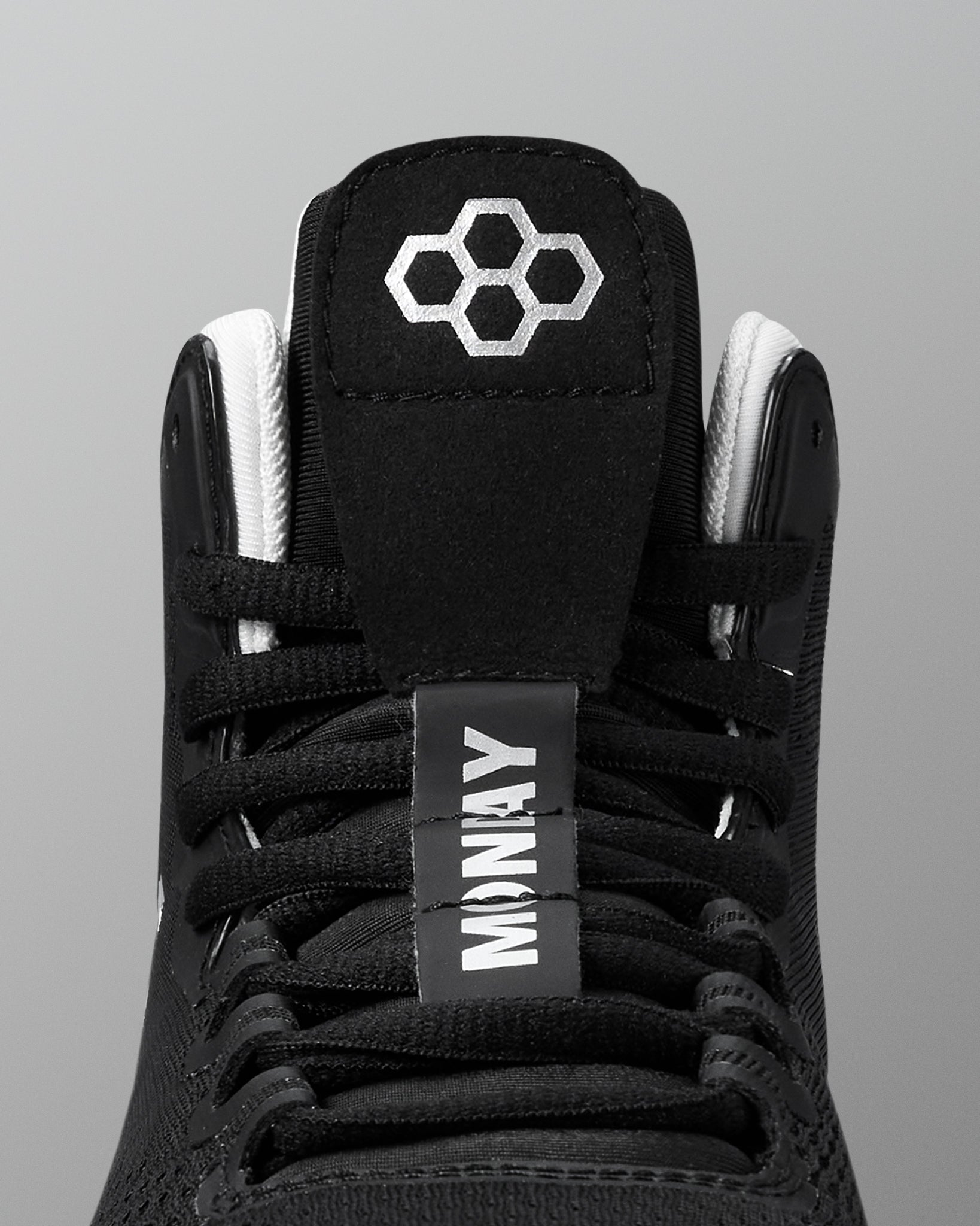 Black wrestling shoe with white laces and a visible brand logo on a gray background