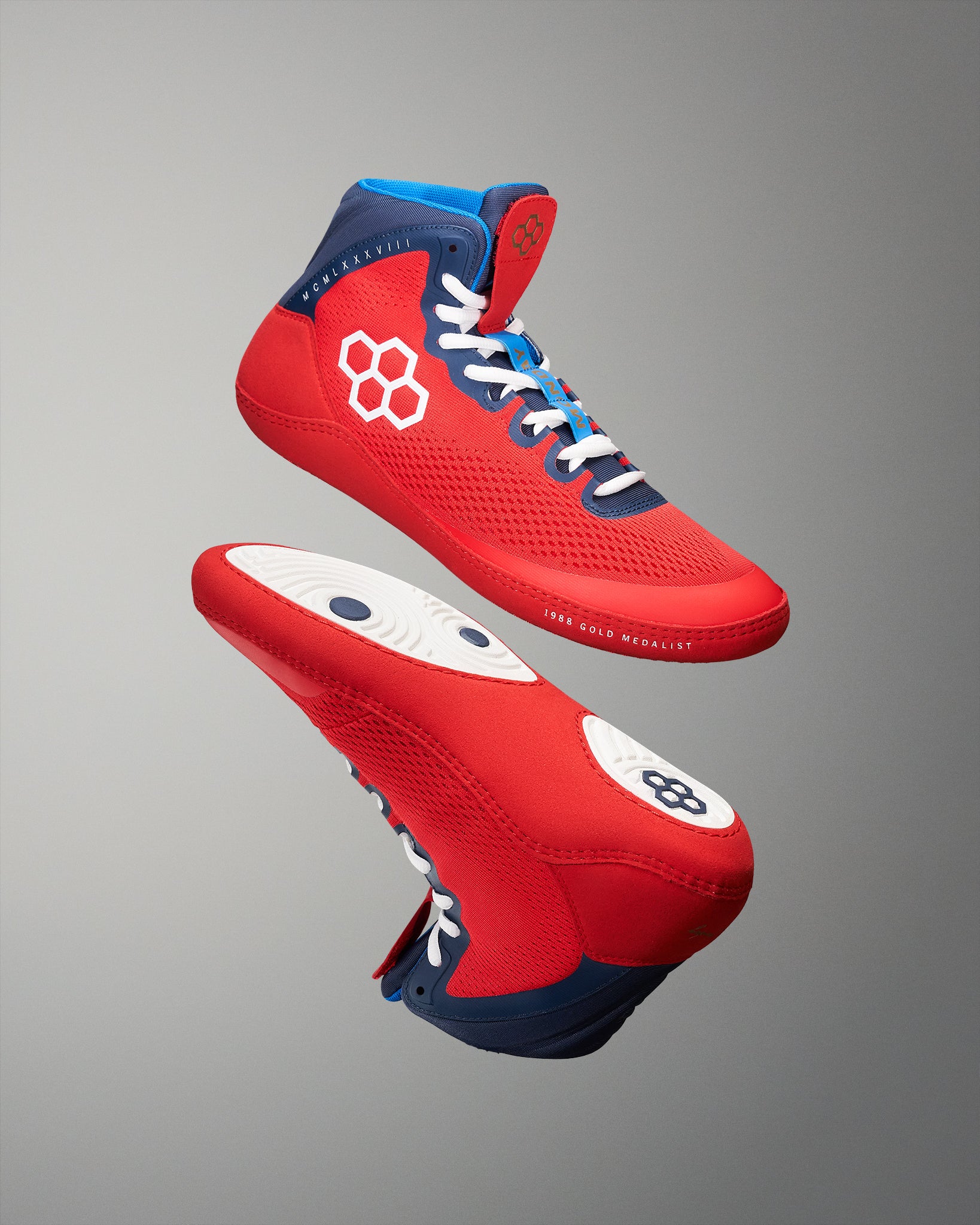 Red wrestling shoes with blue and white accents on a gray background