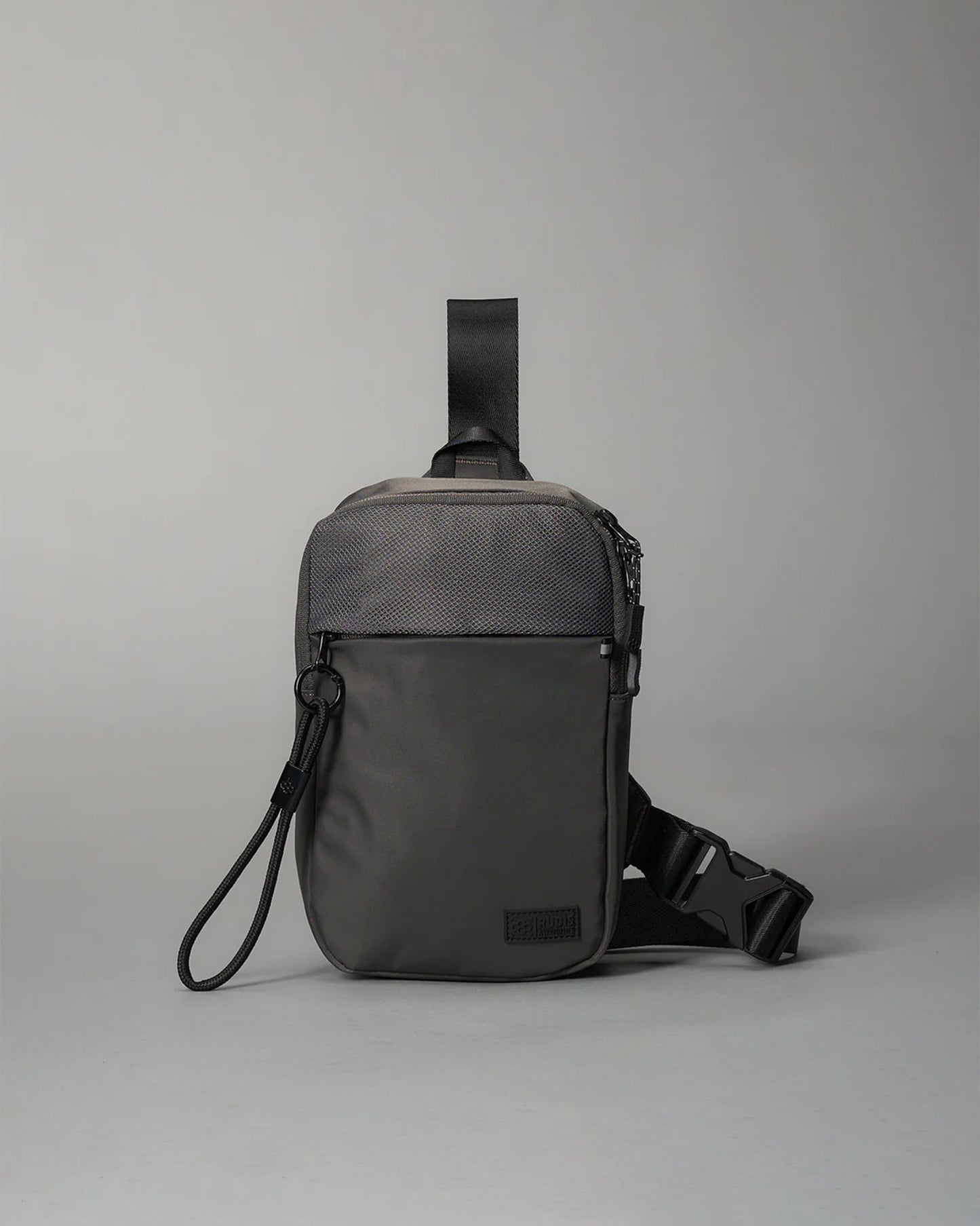 A compact gray shoulder bag with a textured front panel and adjustable strap features a secure zip closure and a smaller front pocket, making it ideal for casual or urban use.