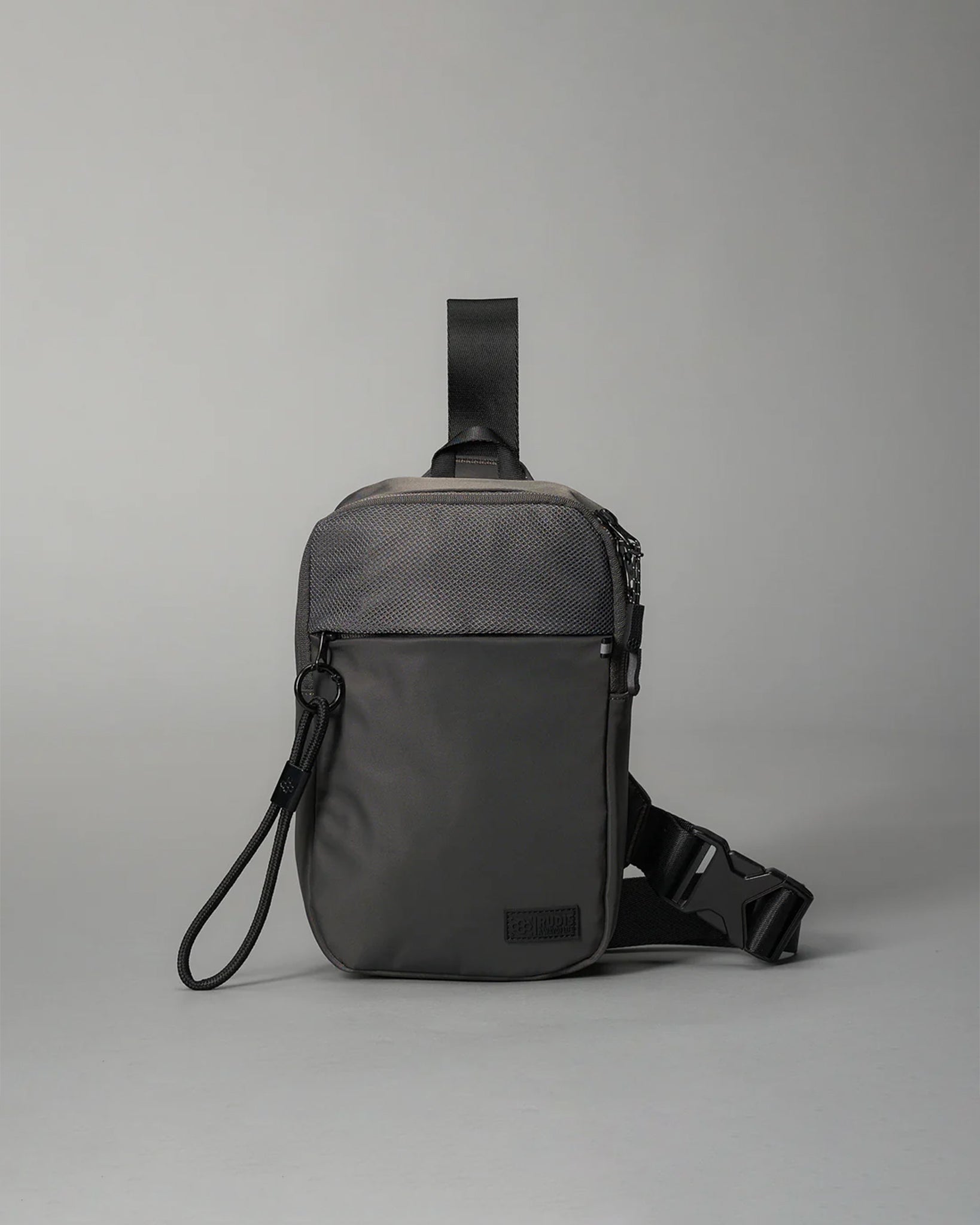 A compact gray shoulder bag with a textured front panel and adjustable strap features a secure zip closure and a smaller front pocket, making it ideal for casual or urban use.