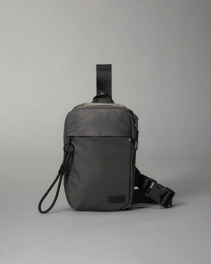 A compact gray shoulder bag with a textured front panel and adjustable strap features a secure zip closure and a smaller front pocket, making it ideal for casual or urban use.