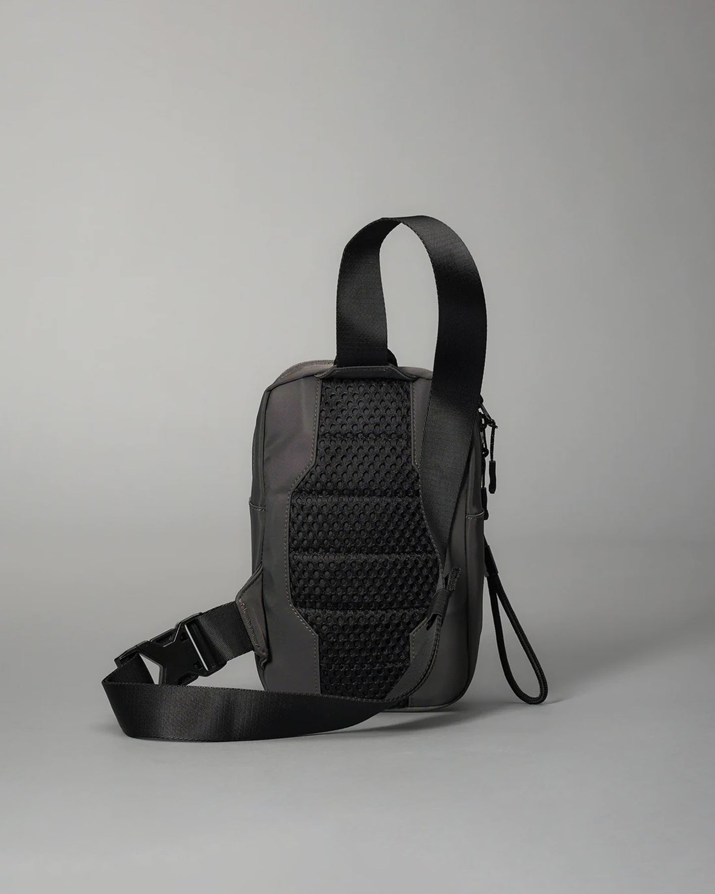 A compact black crossbody bag showcases a textured back for enhanced grip, featuring an adjustable strap for comfort and durability against a light gray background.