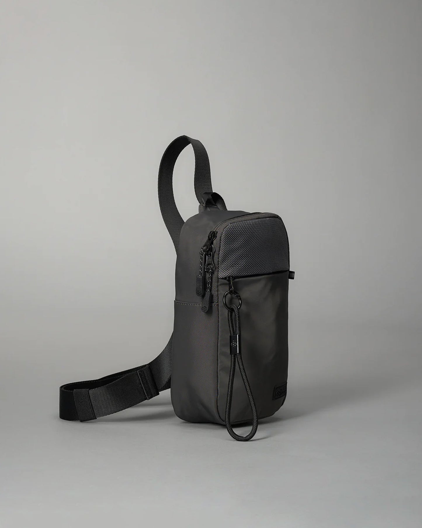 Compact black crossbody bag with a durable strap and secure zippers, designed for casual use or travel, set against a soft gray background.