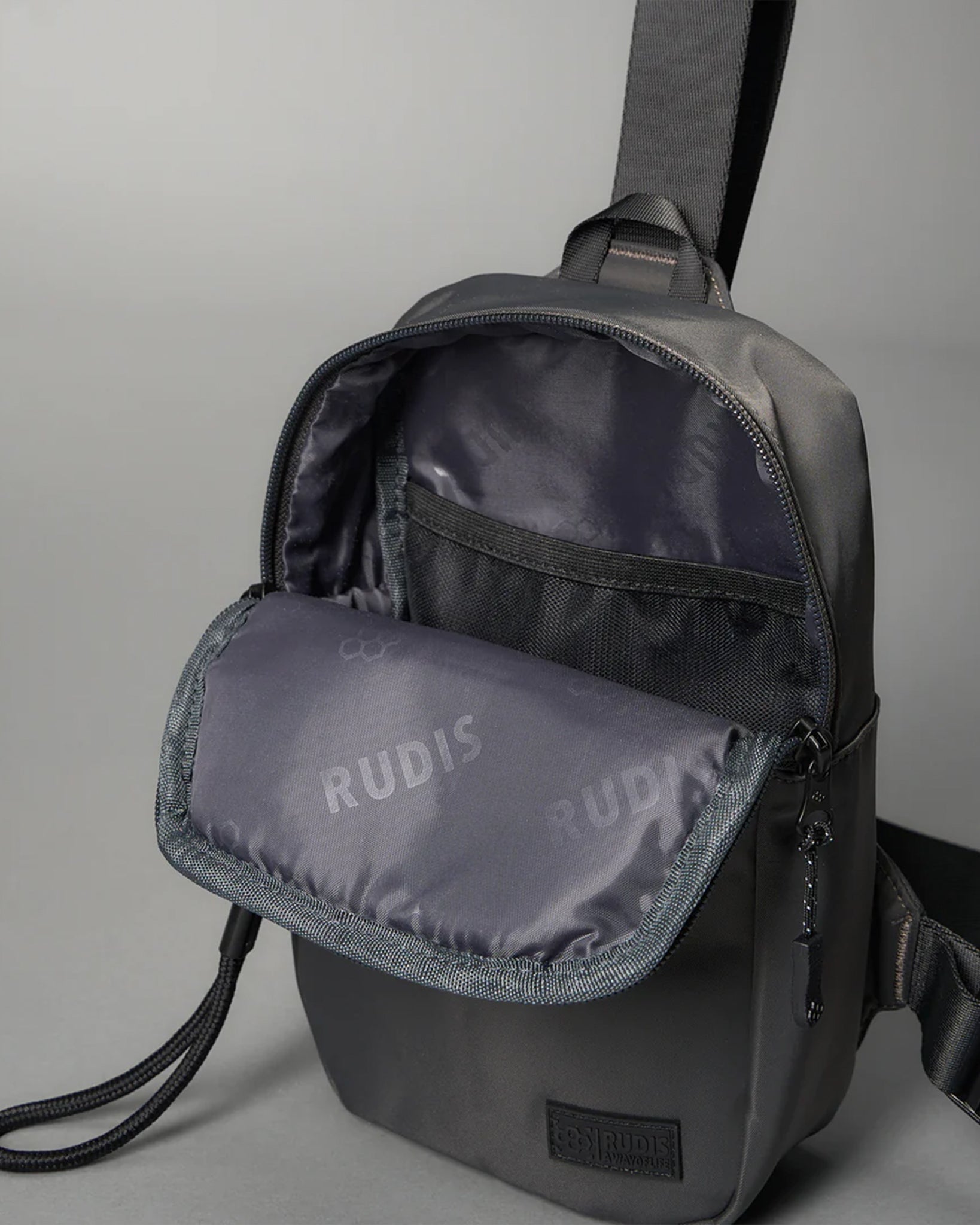 Gray backpack with an opened front pocket revealing a soft interior displaying 'RUDIS' branding, designed for modern functionality.