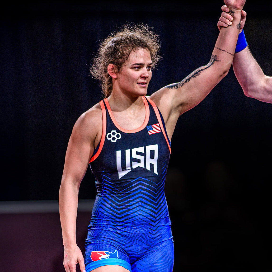 Wrestler Kayla Miracle in a blue USA wrestling singlet celebrating with a raised arm