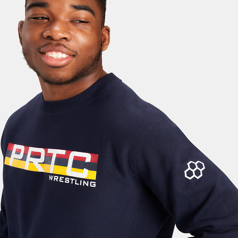 A young man with a joyful expression wearing a navy blue sweatshirt featuring PRTC WRESTLING graphics in bold colors across the chest