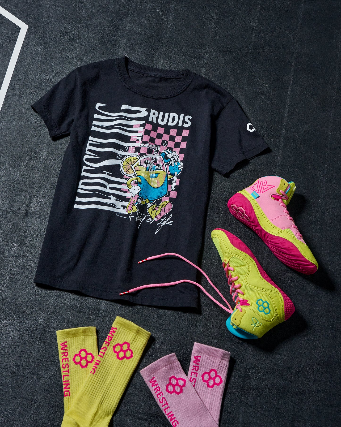 Black t-shirt with graphic design, pink and yellow wrestling shoes, and yellow and pink socks on a dark textured background.
