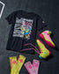 Black t-shirt with graphic design, pink and yellow wrestling shoes, and yellow and pink socks on a dark textured background.